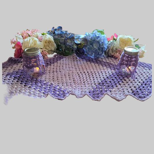 Crocheted table runner with lit candles and flowers on a wooden table.
