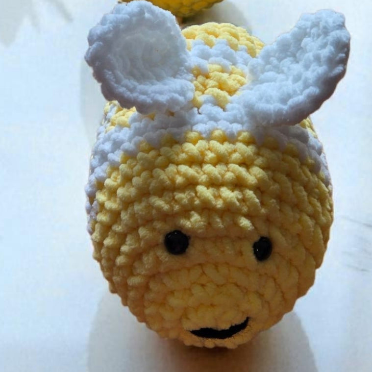 handcrafted yellow and white amigurumi bumblebee plush on reflective surface with small potted plants in background