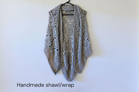 Handmade crochet shawl wrap in elegant cream and gray lightweight design hanging on black hanger