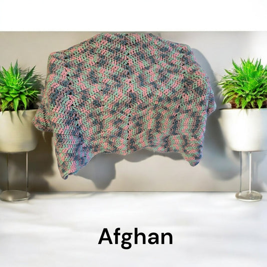 Handmade crocheted Afghan blanket with multicolored design draped between two plants