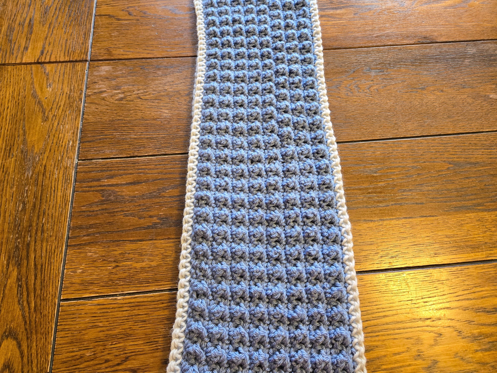 Handmade blue puff stitch winter scarf on wooden surface.