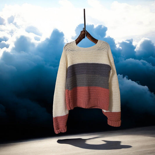 Handmade sweater in cream, light gray, and mauve colors, hangs against a cloudy sky background.