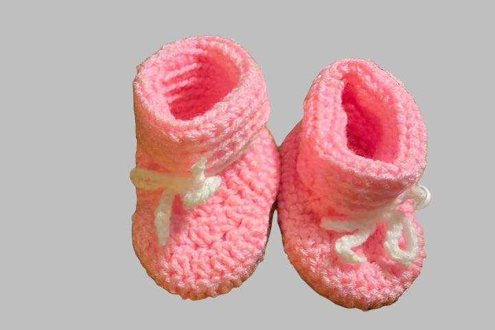 Pink baby booties for newborns with soft knit fabric and white bow accents, size 0-6 months.