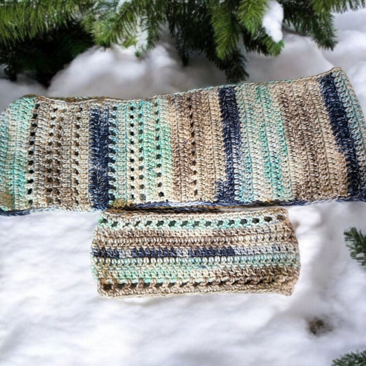 Multicolored handmade scarf and winter headband set displayed on snow.