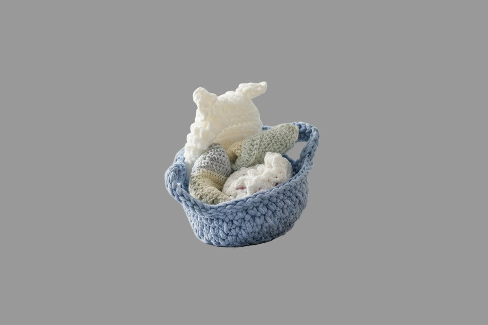 Baby gift basket with blue t-shirt yarn handles including white chunky yarn baby hat with ears, cotton wash cloths, and crocheted cotton bag with baby ducks.