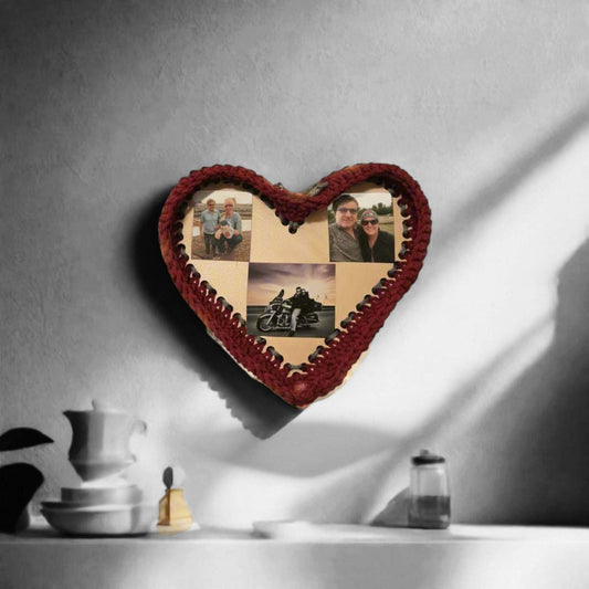 Handmade heart-shaped photo frame with burgundy crochet holding four photos displayed on wall shadowed by sunlight