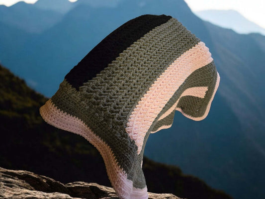 Handmade Afghan blanket in pink, gray, and black colors draped outdoors on rocky surface