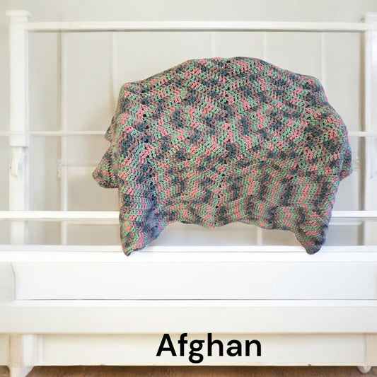 Handmade crocheted Afghan blanket in multicolored yarn draped over white metal bed frame